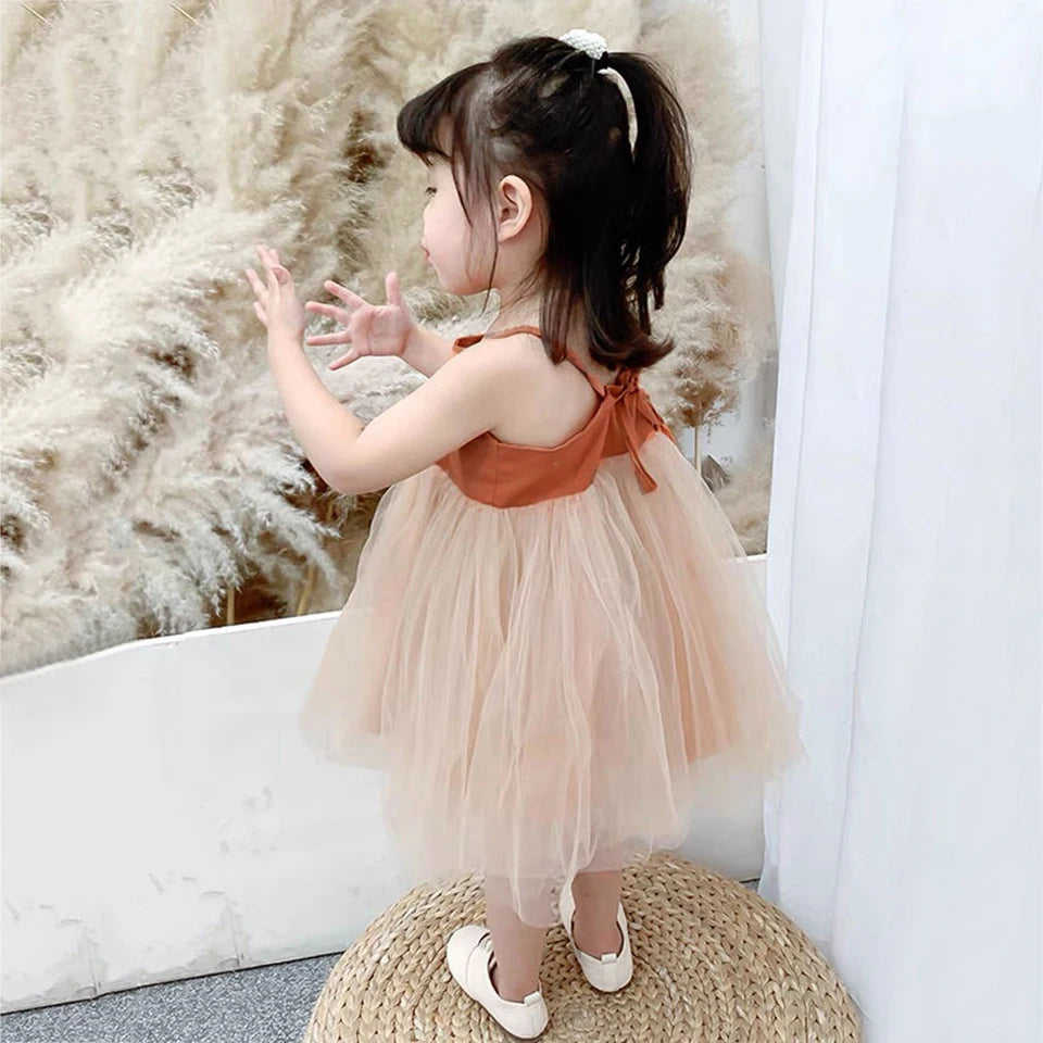 Young girl in a peach dress standing on a woven mat with a neutral background
